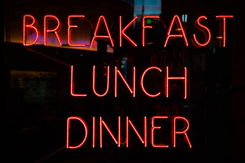 Vibrant red neon signs advertising breakfast, lunch, and dinner glow in a dimly lit establishment in Manhattan, New York. - ADSF52046