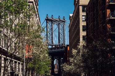 A vibrant street scene in DUMBO, Brooklyn, capturing the iconic Manhattan Bridge framed between two historic brick buildings. - ADSF52050