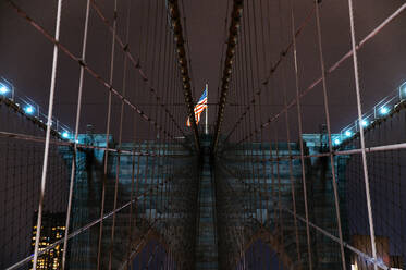 Nachtansicht der Brooklyn Bridge in Manhattan mit der beleuchteten amerikanischen Flagge an prominenter Stelle. - ADSF52054