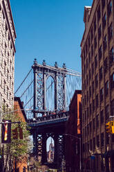 A vibrant street scene in DUMBO, Brooklyn, capturing the iconic Manhattan Bridge framed between two historic brick buildings. - ADSF52064