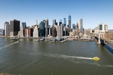 Panoramablick auf die Skyline von Manhattan mit Wolkenkratzern, der Brooklyn Bridge und einem Wassertaxi auf dem Fluss. - ADSF52065