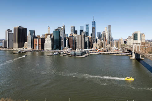 Panoramablick auf die Skyline von Manhattan mit Wolkenkratzern, der Brooklyn Bridge und einem Wassertaxi auf dem Fluss. - ADSF52065