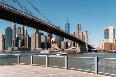 Eine klare Tagesansicht der Skyline von Manhattan mit der Brooklyn Bridge im Vordergrund und einem Boot, das auf dem Hudson River fährt. - ADSF52066