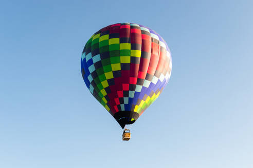 A vibrant, multicolored hot air balloon soars in a clear blue sky during a sunny day - ADSF52074
