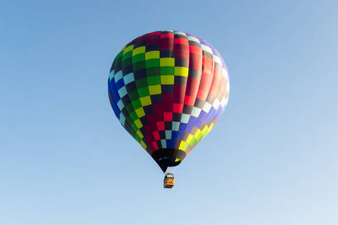 Ein leuchtend bunter Heißluftballon steigt an einem sonnigen Tag in den blauen Himmel auf - ADSF52074