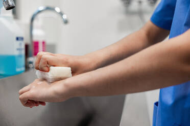 Crop faceless nurse in uniform washing hands with sponge on blurred background of sink at hospital - ADSF52159