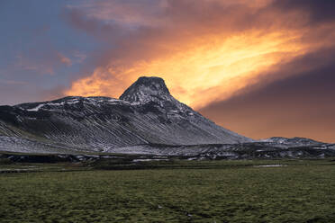 Ein atemberaubender Sonnenuntergang färbt den Himmel mit feurigen Farben hinter einem schneebedeckten Berggipfel in der zerklüfteten Landschaft Islands. - ADSF52169