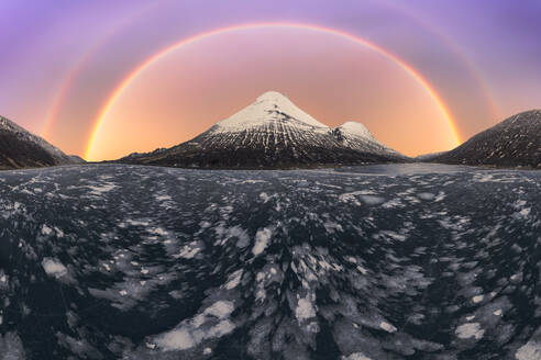 Ein fesselnder doppelter Regenbogen, der eine frostige isländische Landschaft mit einem schneebedeckten Berg im Hintergrund während des Sonnenuntergangs ziert. - ADSF52170