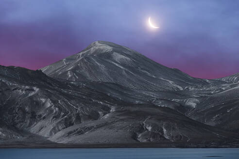 The crescent moon hangs above a serene Icelandic mountain landscape under a twilight sky. - ADSF52172