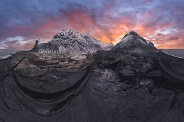 Ein Panoramablick auf die schneebedeckten Berge Islands, während die feurigen Farben des Sonnenuntergangs den Himmel überziehen. - ADSF52175