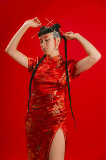 A woman stands confidently in a vibrant red, traditional Chinese dress with gold detailing, posing against a matching red backdrop. - ADSF52207