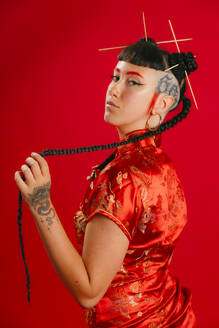 Woman in traditional red cheongsam dress holding her braid against a red background, with a modern twist. - ADSF52208