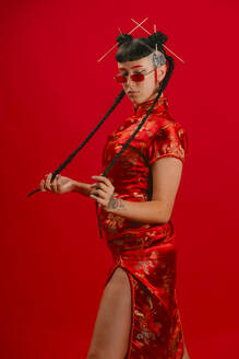 Eine modebewusste Frau posiert in einem roten Cheongsam mit einem modernen Twist vor einem passenden roten Hintergrund, der eine Mischung aus Tradition und modernem Stil darstellt. - ADSF52211