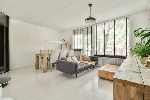 Ein einladendes, modernes Wohnzimmer mit minimalistischem Design, grauem Sofa, Holzmöbeln und viel natürlichem Licht durch große Fenster. - ADSF52227