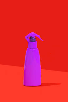 Ein minimalistisches Bild mit einer lilafarbenen Sprühflasche mit einem Abzug vor einem auffälligen roten Hintergrund, der einen starken Farbkontrast erzeugt. - ADSF52268