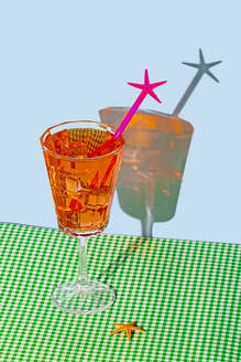 An elegant orange cocktail with a pink star stirrer stands on a green checkered cloth against a pale blue background, casting a playful shadow - ADSF52270