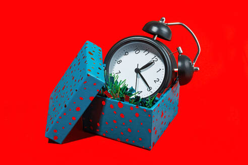 Ein schwarzer Vintage-Wecker, eingebettet in eine offene, blau gepunktete Geschenkbox vor rotem Hintergrund. - ADSF52272