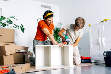 Teenager in Freizeitkleidung hilft seiner Mutter beim Zusammenbau von Kartons während des Umzugs in eine neue Wohnung - ADSF52320