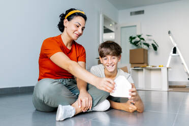 Cheerful parent in casual clothes sitting with son and reading funny message on present while relaxing during relocation - ADSF52324