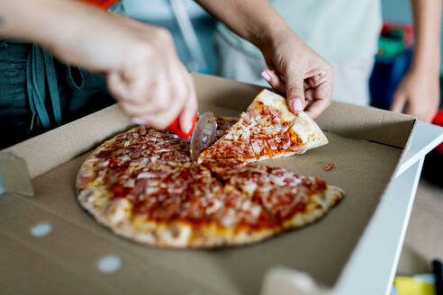 Hohe Winkel weichen Fokus Blick auf anonyme Person Schneiden leckere Pizza in offenen Karton mit rotem Messer - ADSF52331