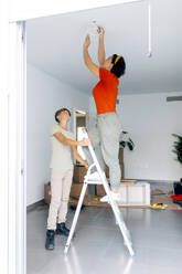 Germany, Cologne, Mature woman balancing on ladder during painting gable  roof stock photo