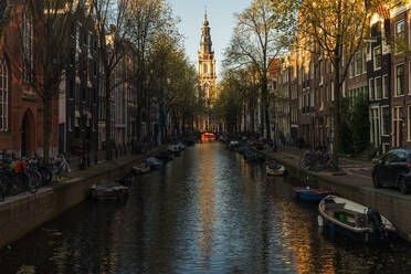 Warmes Sonnenuntergangslicht auf dem Amsterdamer Kanal mit vertäuten Booten und traditionellen niederländischen Häusern - ADSF52379