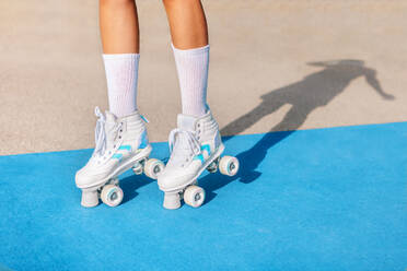 Anonymous of crop black female legs in white socks and quad roller sneakers standing on blue and beige colored sports ground with shadow on sunny day - ADSF52405