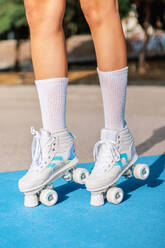 Crop schwarze weibliche Beine in weißen Socken und Quad Roller Turnschuhe stehen auf blau und beige farbigen Sportplatz mit Schatten auf sonnigen Tag - ADSF52406