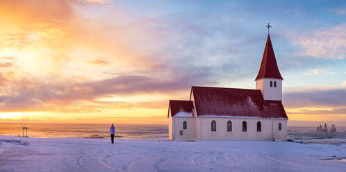 Anonyme Person, die gemeinsam den Sonnenuntergang in einem kleinen isländischen Dorf mit einer Kirche zwischen dem Meer beobachtet - ADSF52436