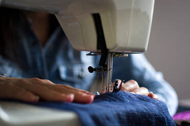 Close-up view of hands sewing denim fabric on a sewing machine, highlighting the needle and thread. - ADSF52489