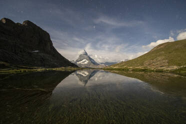 A serene night landscape showcasing the majestic mountain peak reflected in the calm waters of a mountain lake under a starry sky - ADSF52514