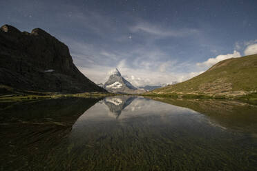 Eine ruhige nächtliche Landschaft, in der sich der majestätische Berggipfel im ruhigen Wasser eines Bergsees unter dem Sternenhimmel spiegelt - ADSF52514