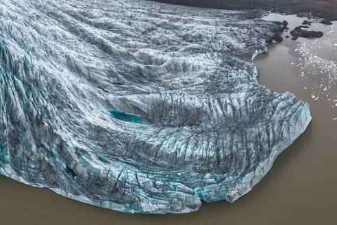 Luftaufnahme von oben, die einen Gletscher zeigt, der durch den Vatnajokull-Nationalpark in Island fließt, umgeben von zerklüftetem Gelände - ADSF52531