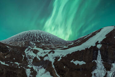 Picturesque view of mountain range covered with snow against blue sky with green aurora borealis in winter - ADSF52537