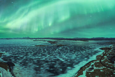 Ein atemberaubender Blick auf das Nordlicht, das über einen sternenklaren Nachthimmel tanzt, über einer ruhigen, schneebedeckten Berglandschaft im Vatnajokull-Nationalpark, Island - ADSF52542