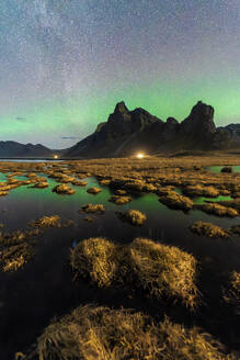 Ein atemberaubender nächtlicher Blick auf das Nordlicht über einem zerklüfteten, von Feuchtgebieten umgebenen Berg in Eystrahorn, Island - ADSF52543