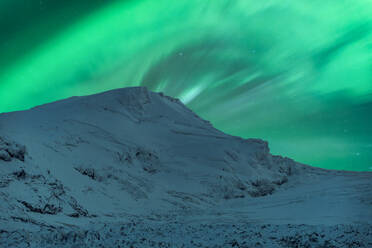 Malerischer Blick auf eine schneebedeckte Bergkette vor blauem Himmel mit grünem Polarlicht im Winter - ADSF52548