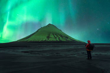 Back view of unrecognizable person standing before a volcano under the vibrant aurora borealis in Iceland - ADSF52549