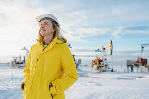 Smiling engineer standing at oil production field in winter - OLRF00101