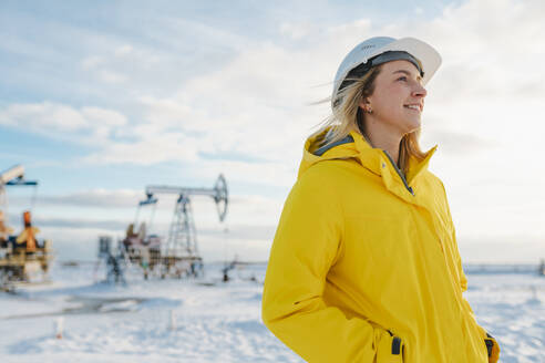 Lächelnder junger Ingenieur auf einem Ölförderfeld im Winter - OLRF00102