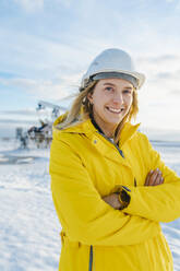 Lächelnder Ingenieur mit verschränkten Armen auf einem Ölförderfeld im Winter - OLRF00106