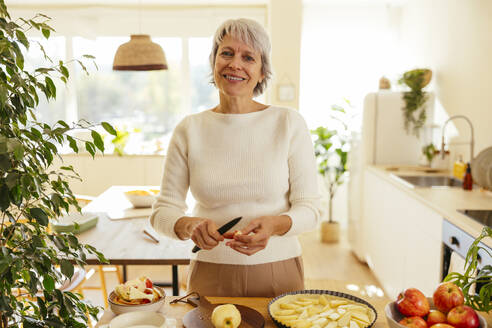 Glückliche Frau bei der Zubereitung von Apfelkuchen in der Küche zu Hause - EBSF04330