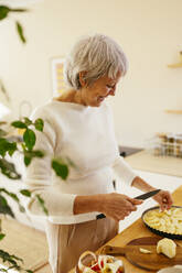 Lächelnde reife Frau schneidet Apfel für Kuchen in der Küche - EBSF04332