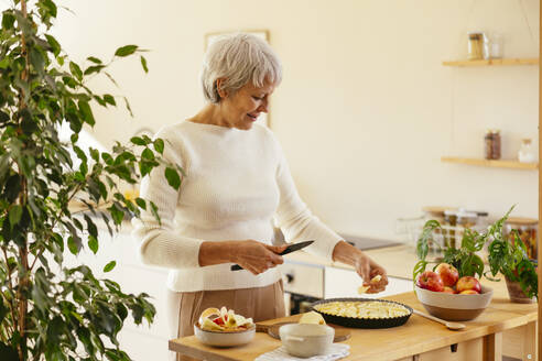 Lächelnde reife Frau schneidet Äpfel für Kuchen in der Küche zu Hause - EBSF04333
