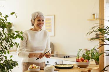 Happy mature woman cutting apple for pie in kitchen - EBSF04334