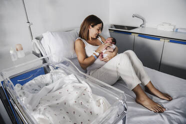 Glückliche Mutter hält ihre kleine Tochter im Krankenhausbett - EBBF08272