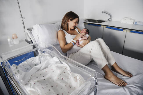 Happy mother holding baby daughter on hospital bed - EBBF08272
