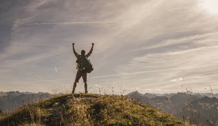 Man standing on mountain top with arms raised in Tannheimer Tal, Tyrol, Austria - UUF30992