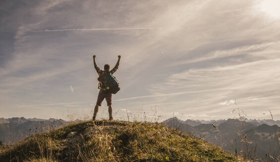 Mann steht mit erhobenen Armen auf einem Berggipfel im Tannheimer Tal, Tirol, Österreich - UUF30992