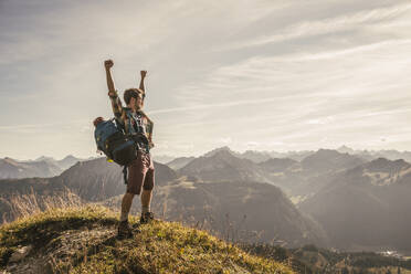 Young man standing on mountain top with arms raised in Tannheimer Tal, Tyrol, Austria - UUF30993